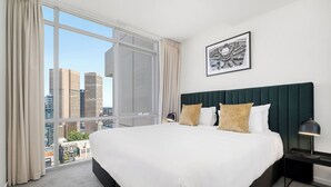 A hotel room with a large bed, a view of city buildings, and a framed picture on the wall.