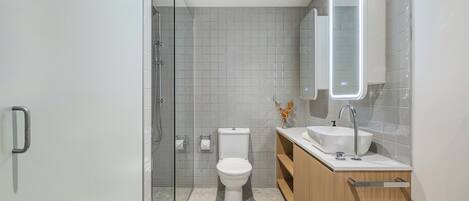 A modern bathroom with a glass-enclosed shower, a toilet, and a vanity with a sink and mirror.