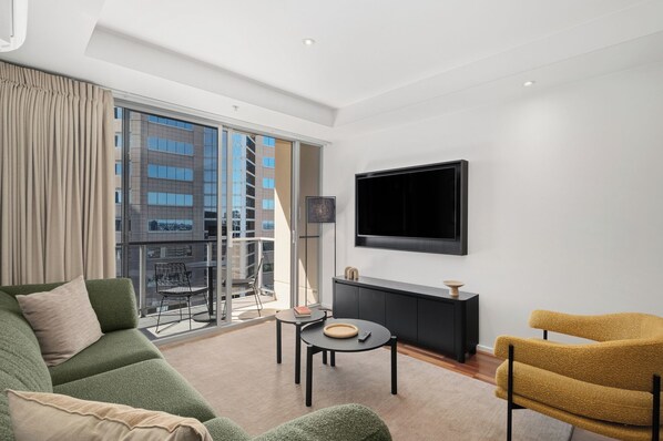 A modern living room with a sofa, a yellow armchair, a coffee table, and a flat-screen TV mounted on the wall.