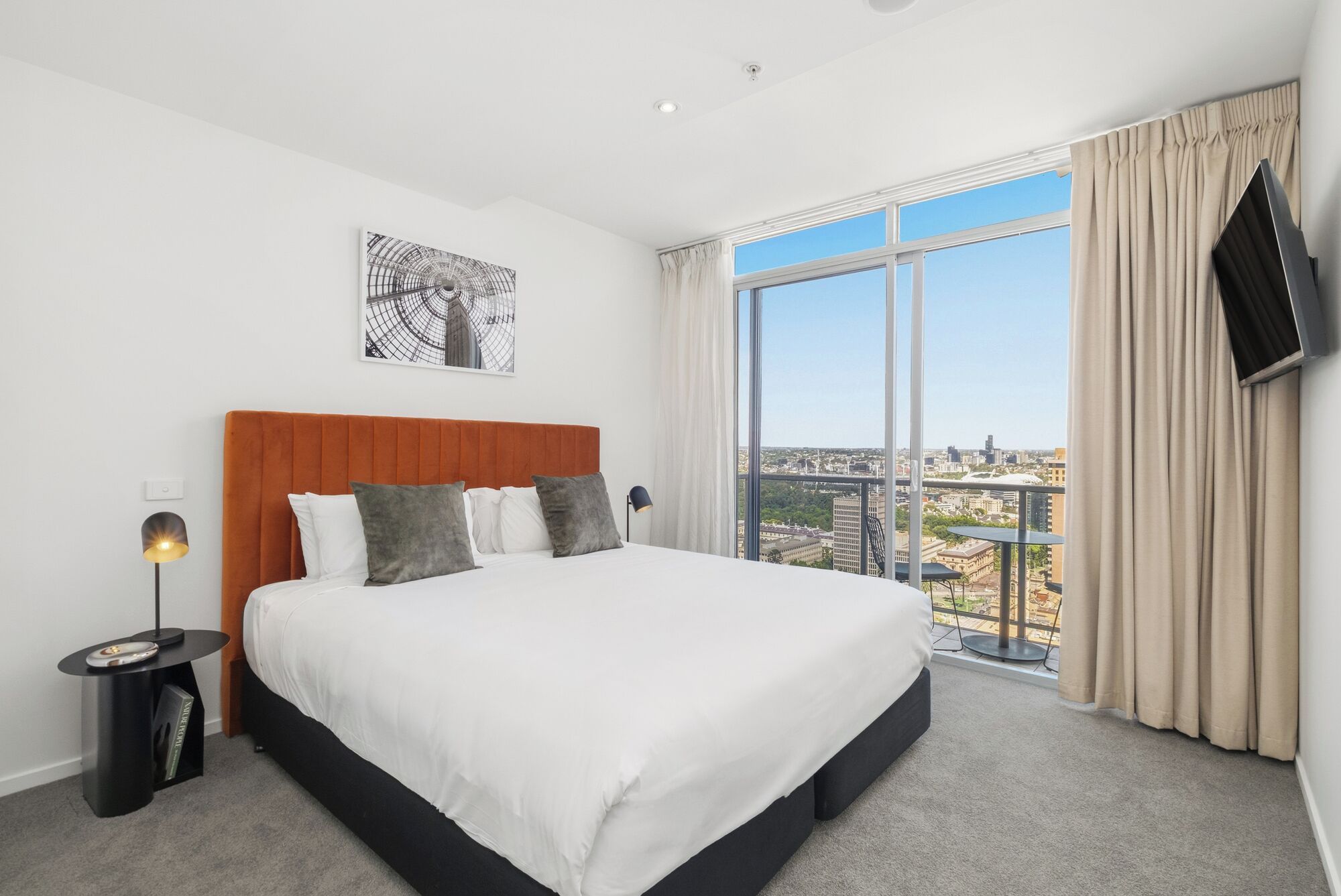 Habitación de hotel moderna con una cama grande, vistas a la ciudad y un televisor de pantalla plana montado en la pared.