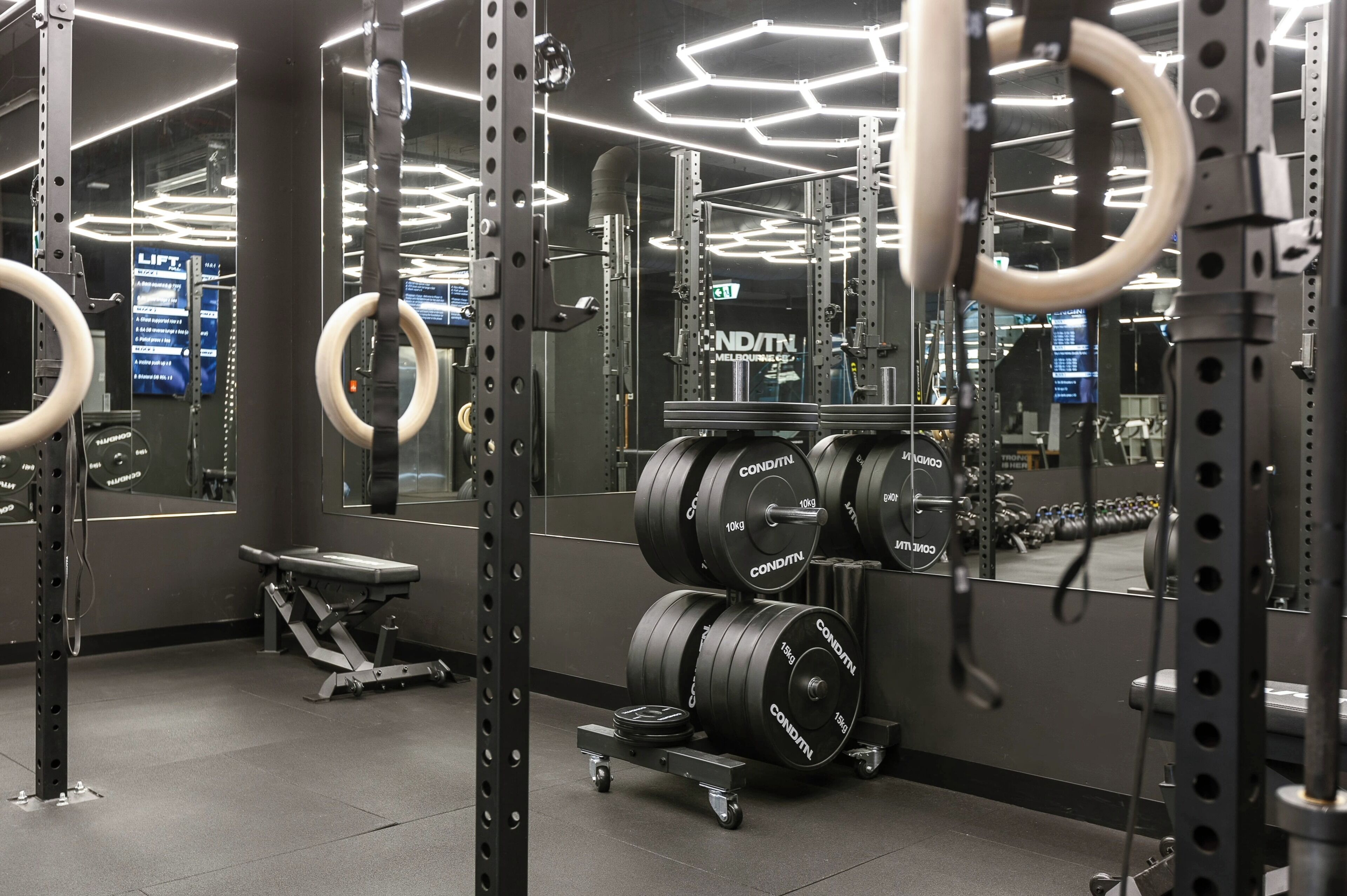 A gym with weightlifting equipment, mirrors, and a bench.