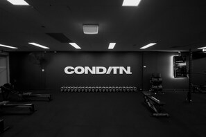 Uma academia com uma placa na parede que diz 'COND/TN', equipamentos de exercícios e um teto com luminárias retangulares.
