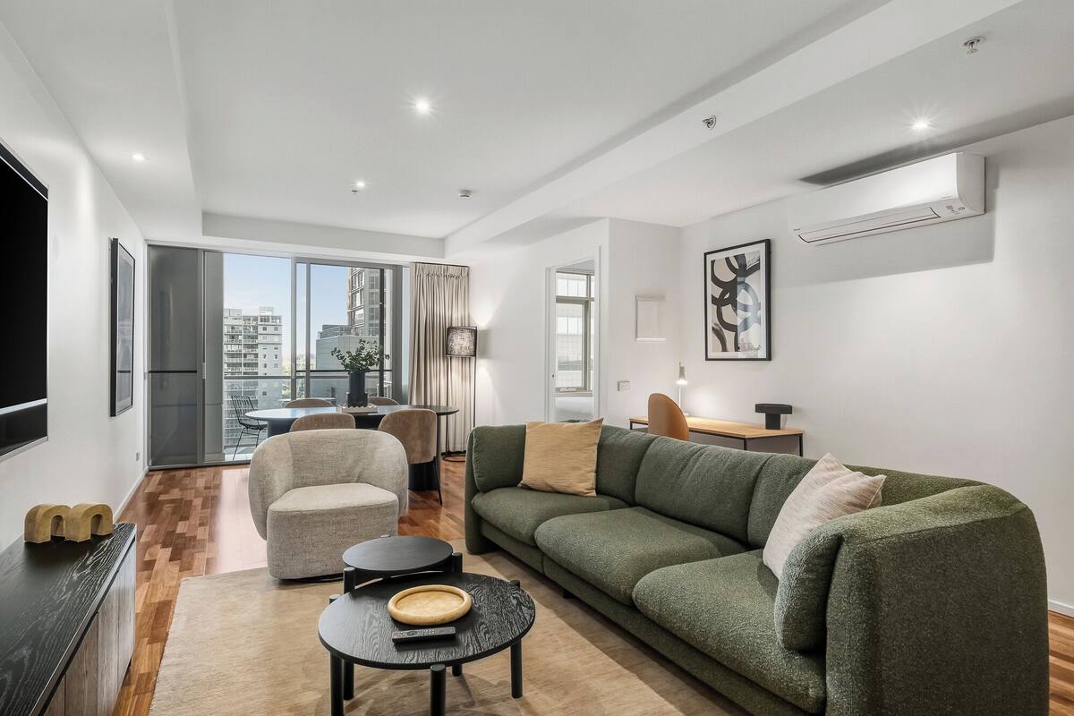 A modern living room with a green sofa, a round coffee table, and a dining area with a table and chairs.