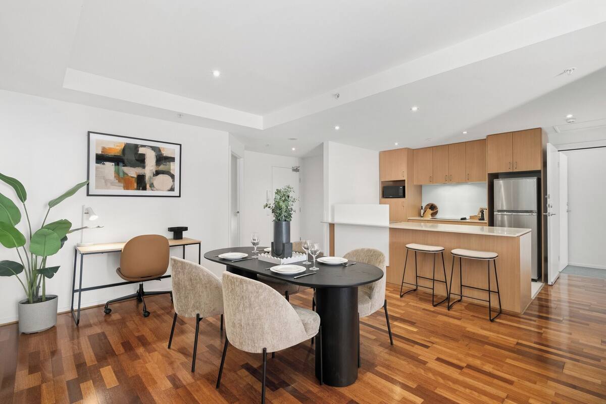 A modern kitchen with wooden cabinets, a stainless steel refrigerator, and a dining area with a black table and chairs.
