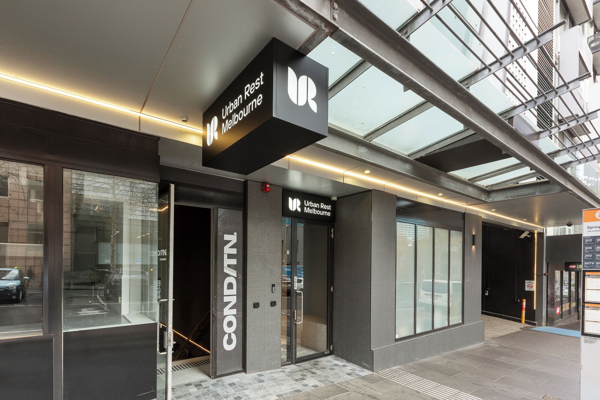 A modern building with a glass facade and a sign for 'Urban Rest Melbourne.'