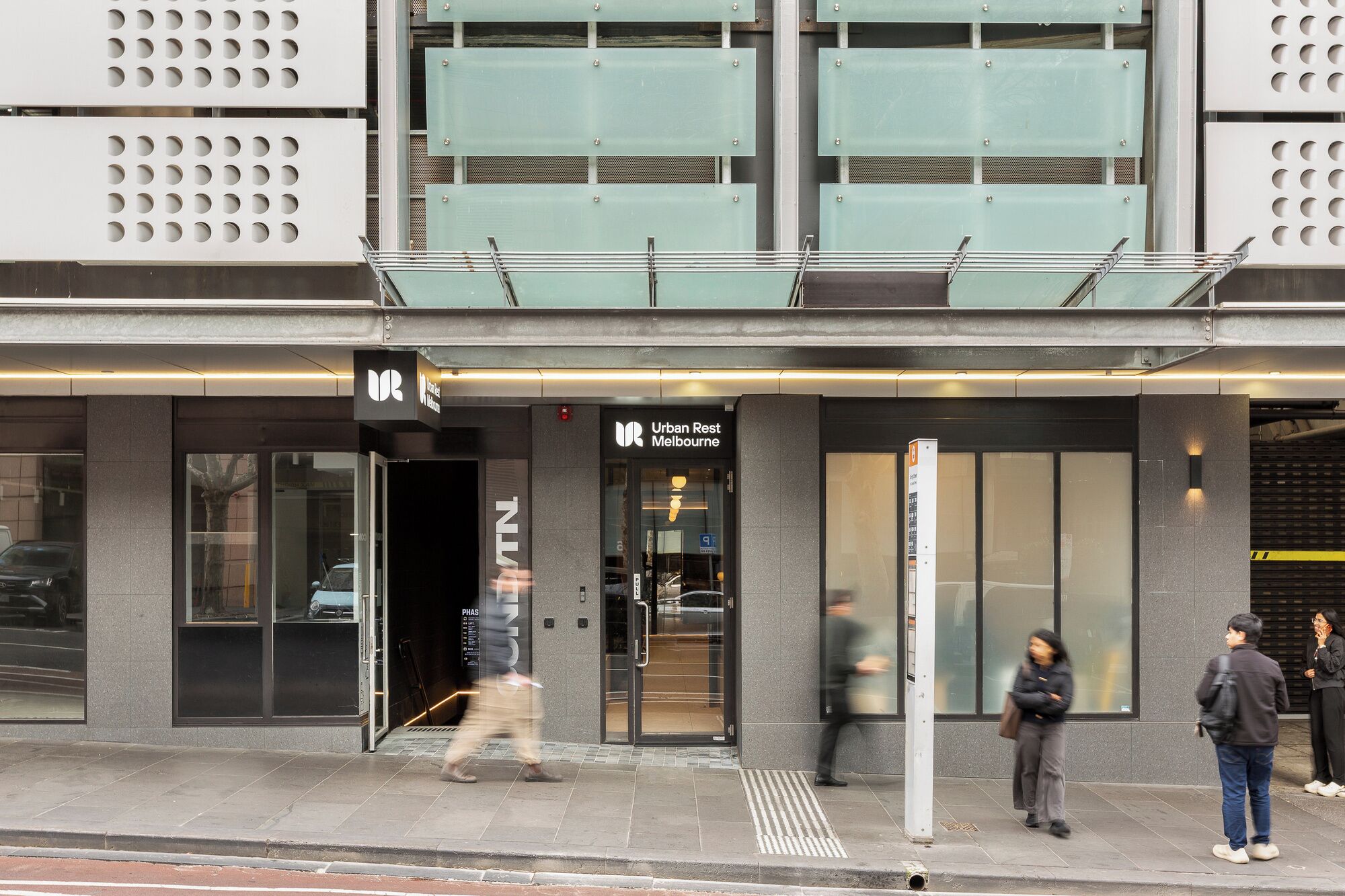 A building with a modern facade, a visible entrance, and a sign for 'Urban Rest Melbourne.'