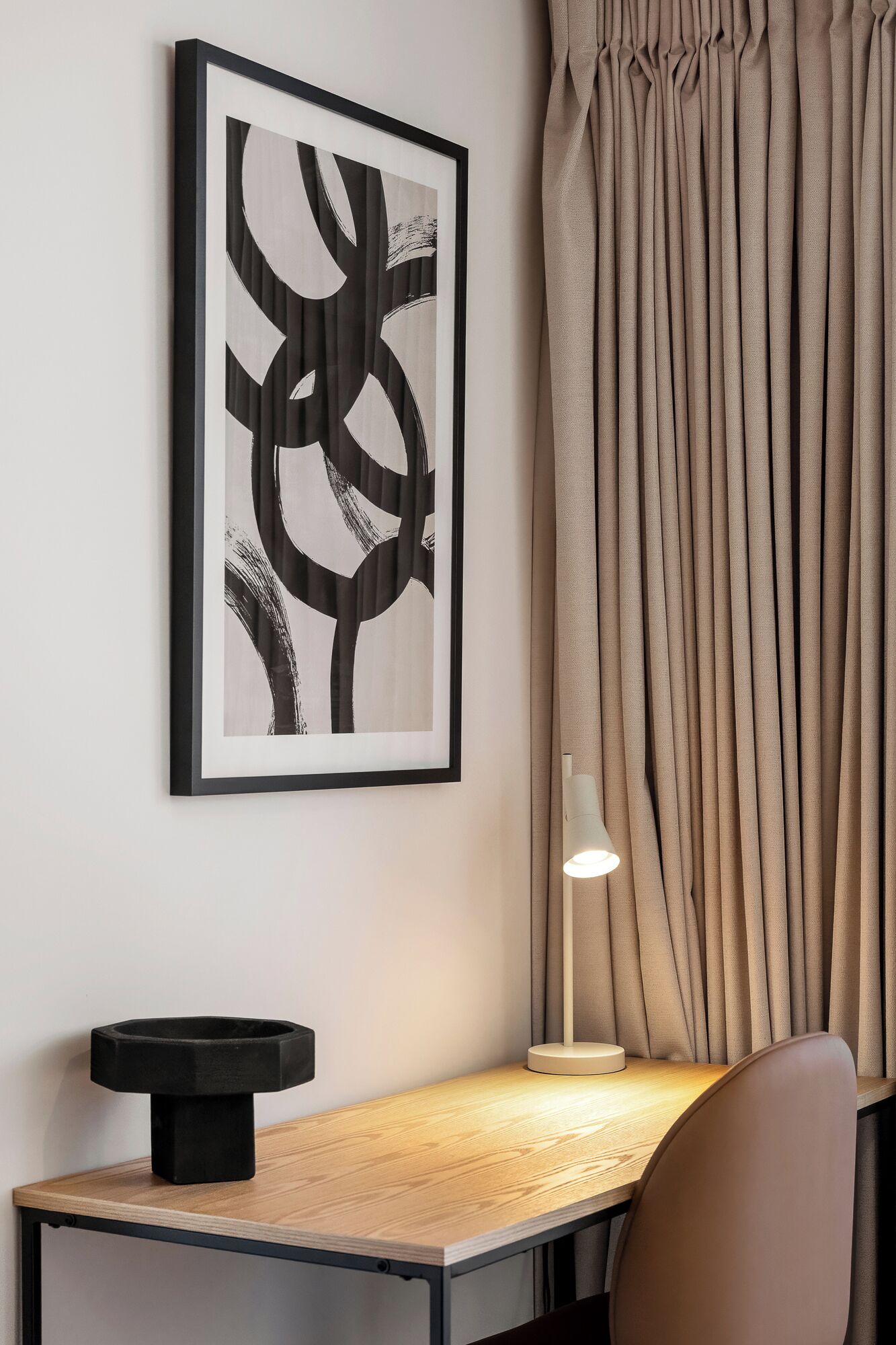 Een moderne kamer met een lijstwerk abstract kunstwerk aan de muur, een bureau met een lamp en een stoel.