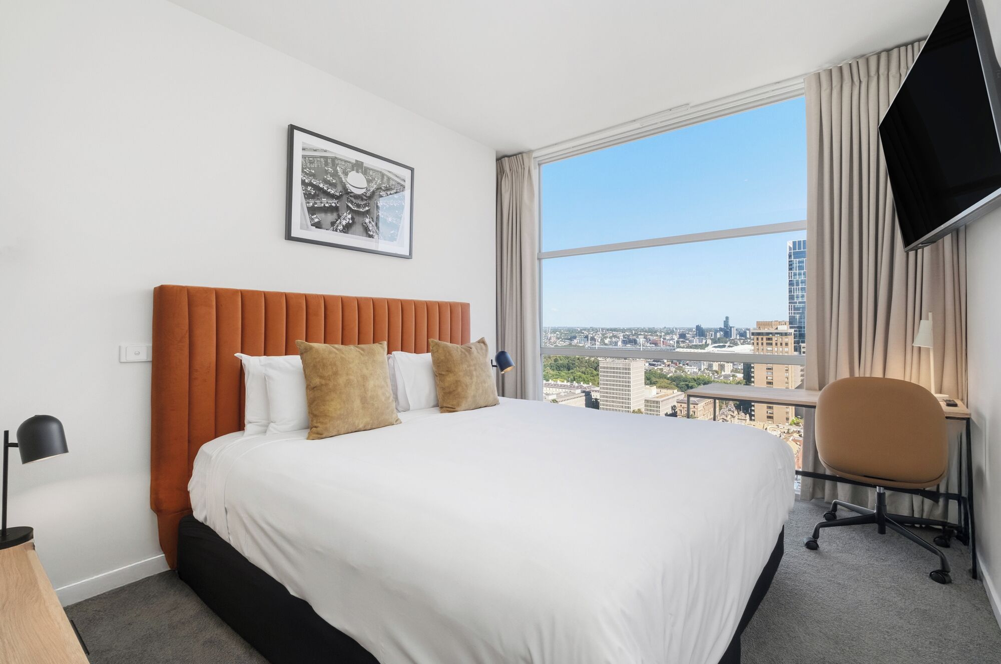 Habitación de hotel con una cama grande, un escritorio, una silla, un televisor y vistas a la ciudad.