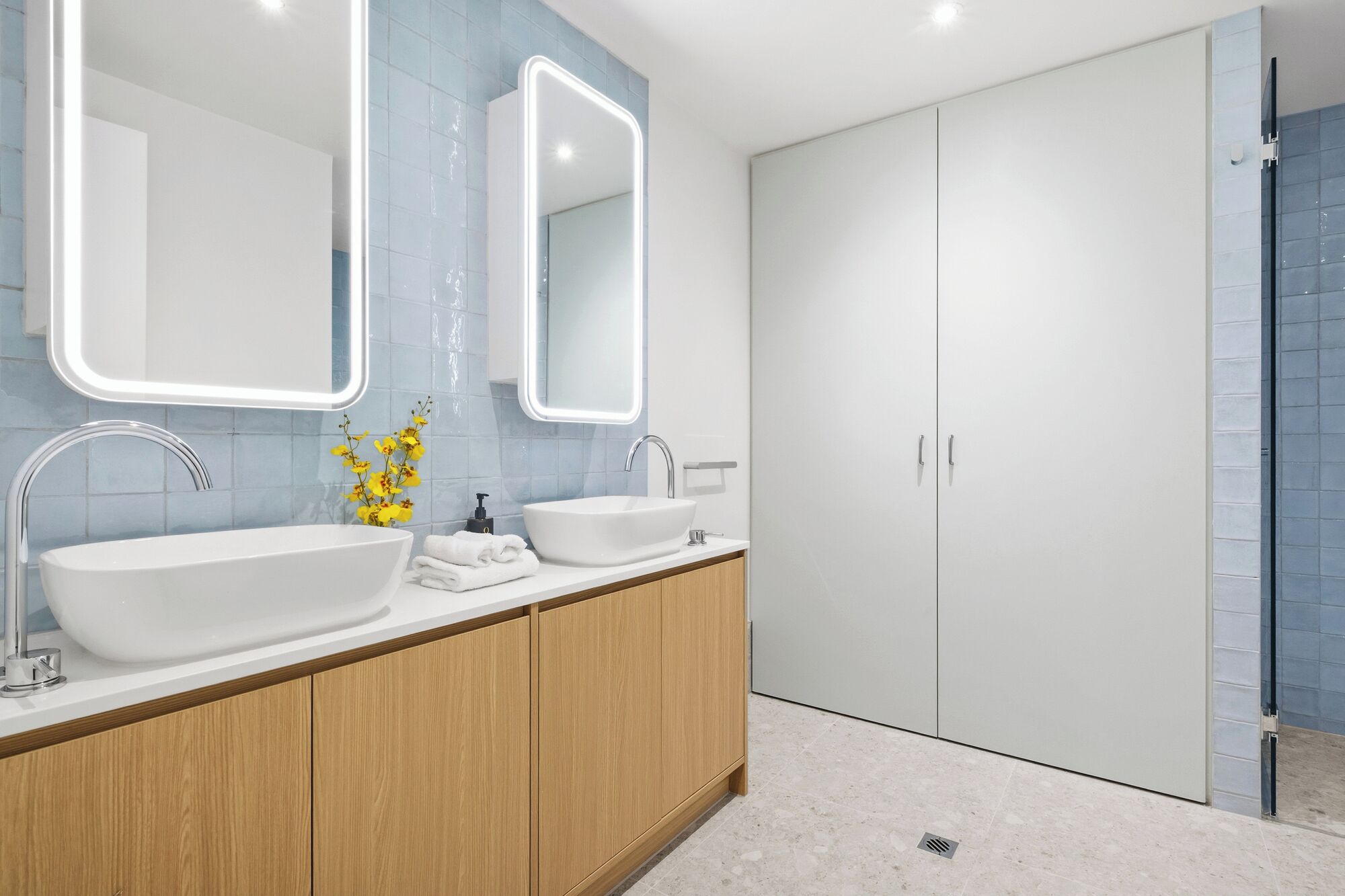 Un baño moderno con dos lavamanos, un espejo grande y una ducha a ras de suelo.