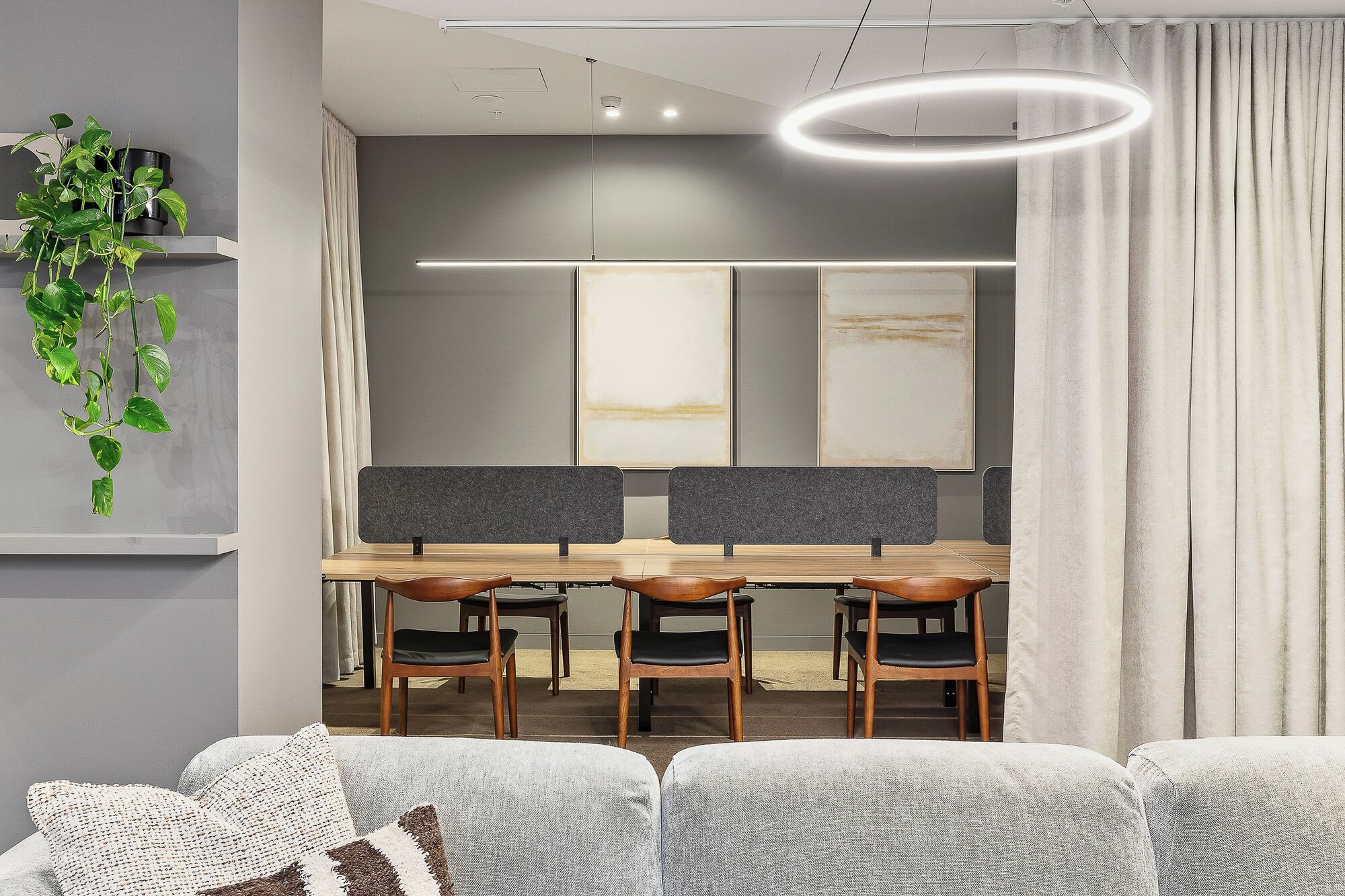 Een moderne eetruimte met een lange tafel, houten stoelen en een plant aan de muur.