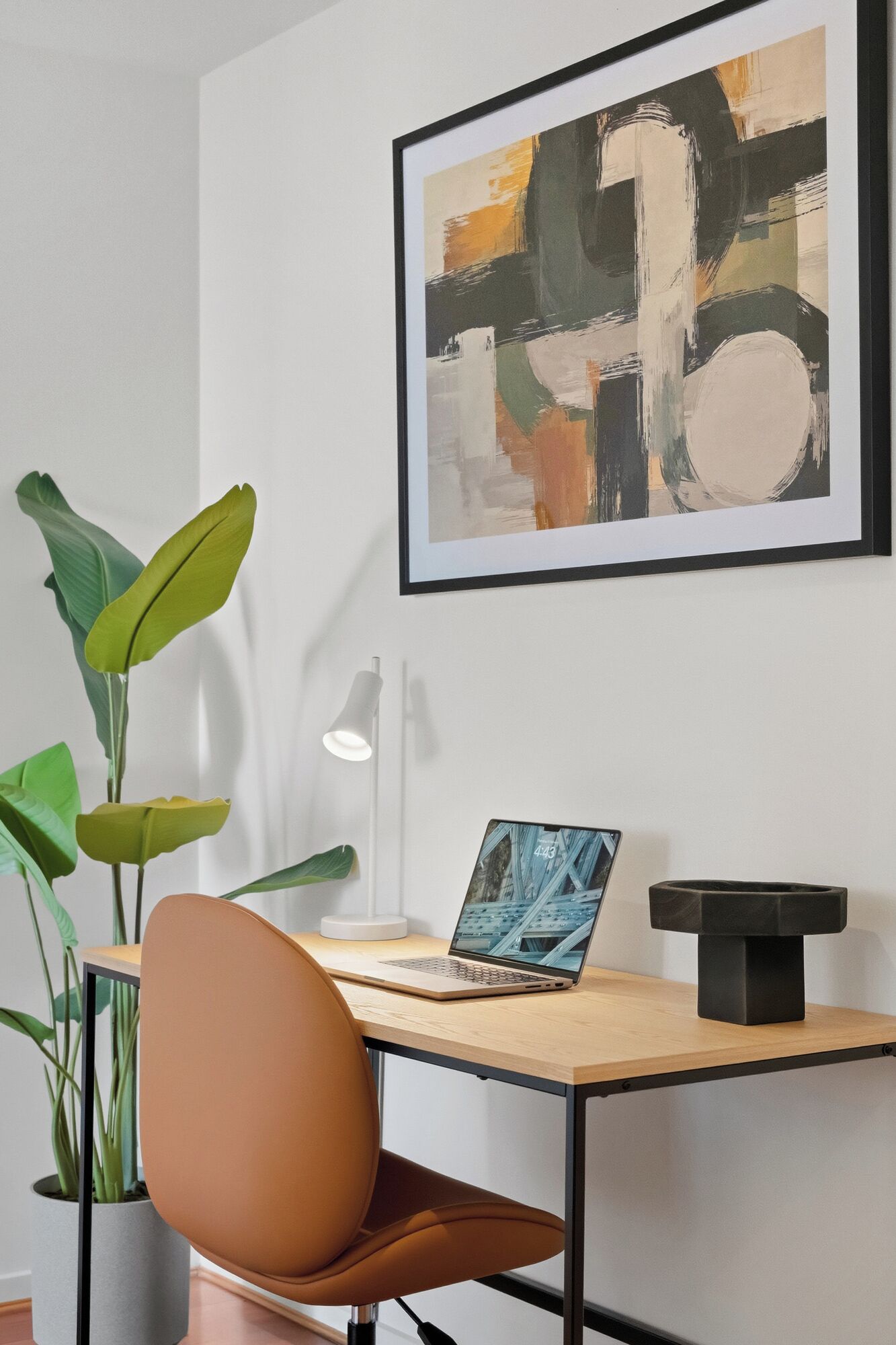 Een moderne kantoorruimte met een houten bureau, een laptop, een groot abstract schilderij en groene planten.