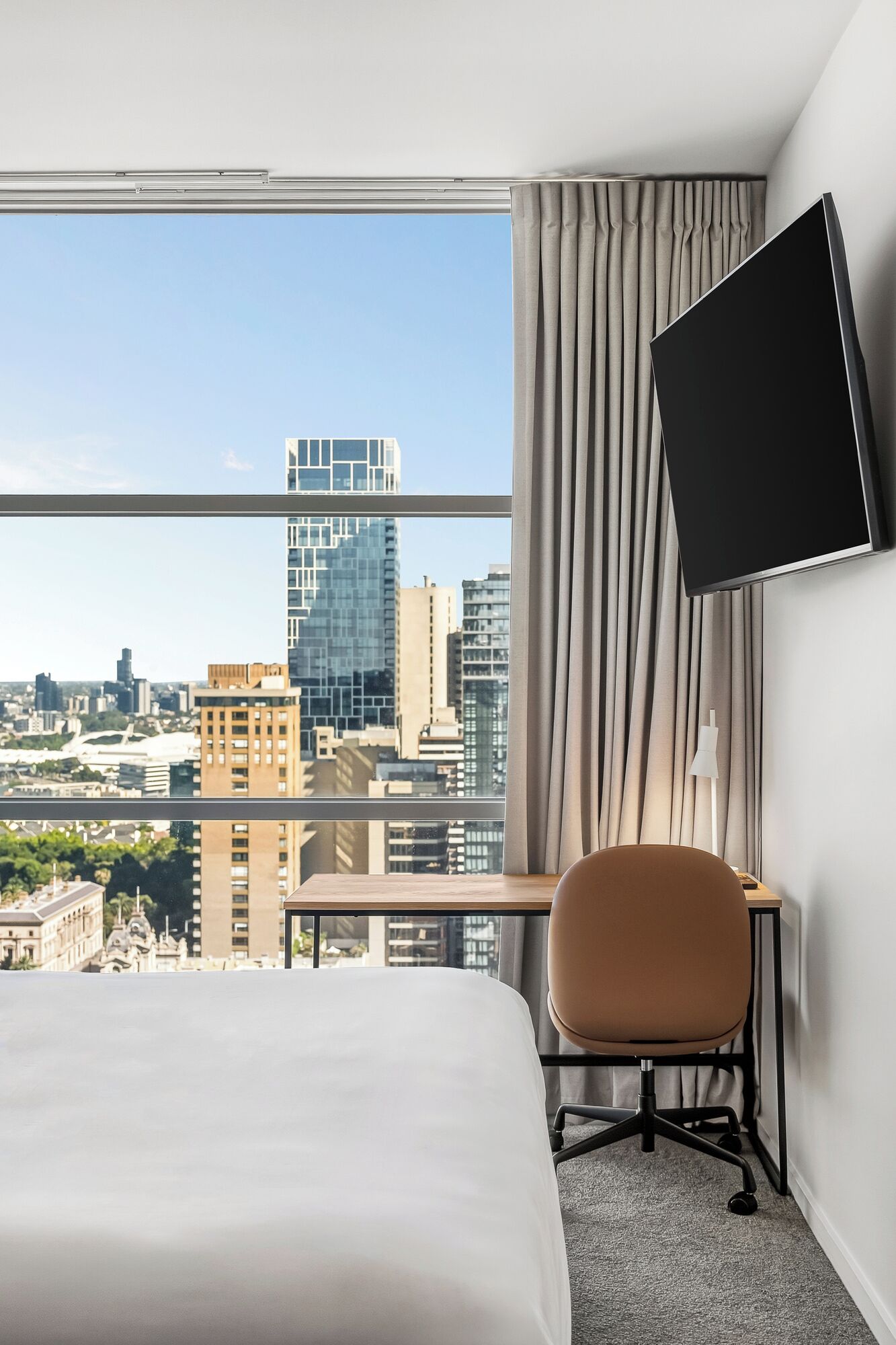 A hotel room with a bed, a desk, a chair, a TV, and a city view.