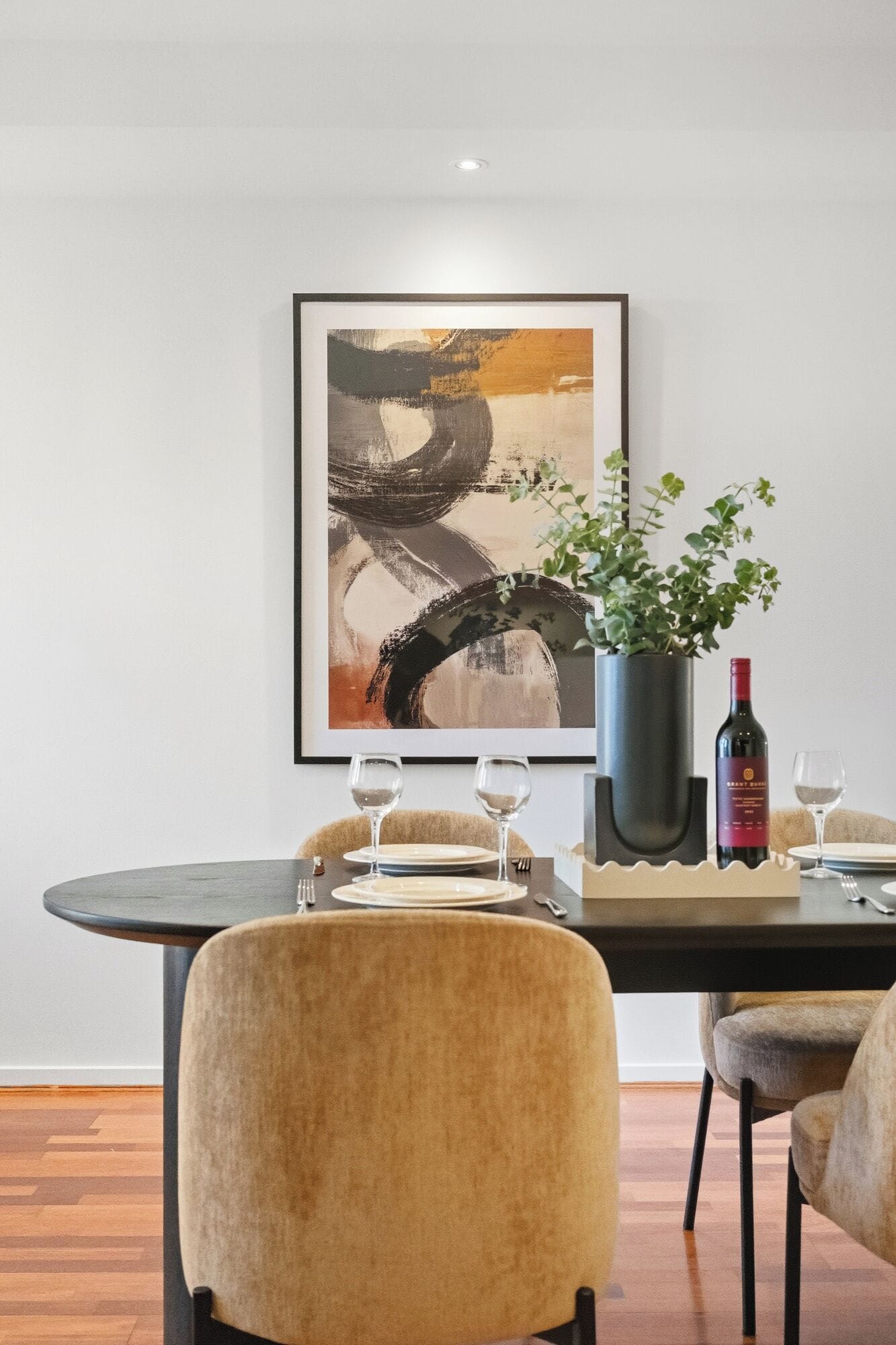 Un comedor con una mesa moderna, dos sillas, una botella de vino y un florero con una planta.