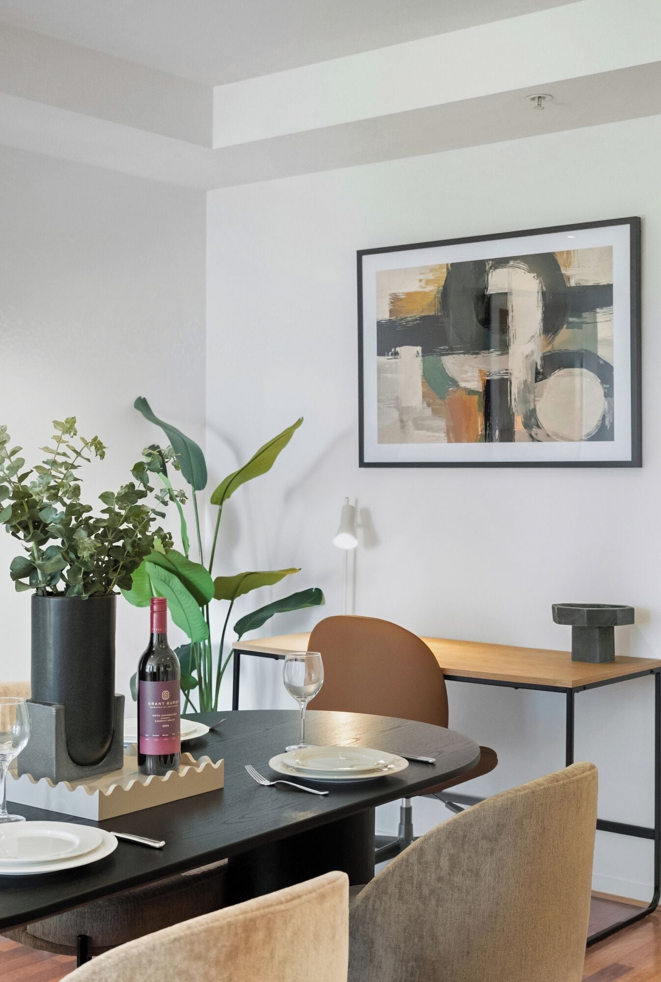 Uma área de refeições com uma mesa redonda, cadeiras, uma garrafa de vinho e um vaso com planta.