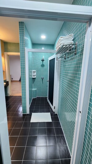 Un baño con azulejos verde mar, una ducha y un lavamanos blanco.