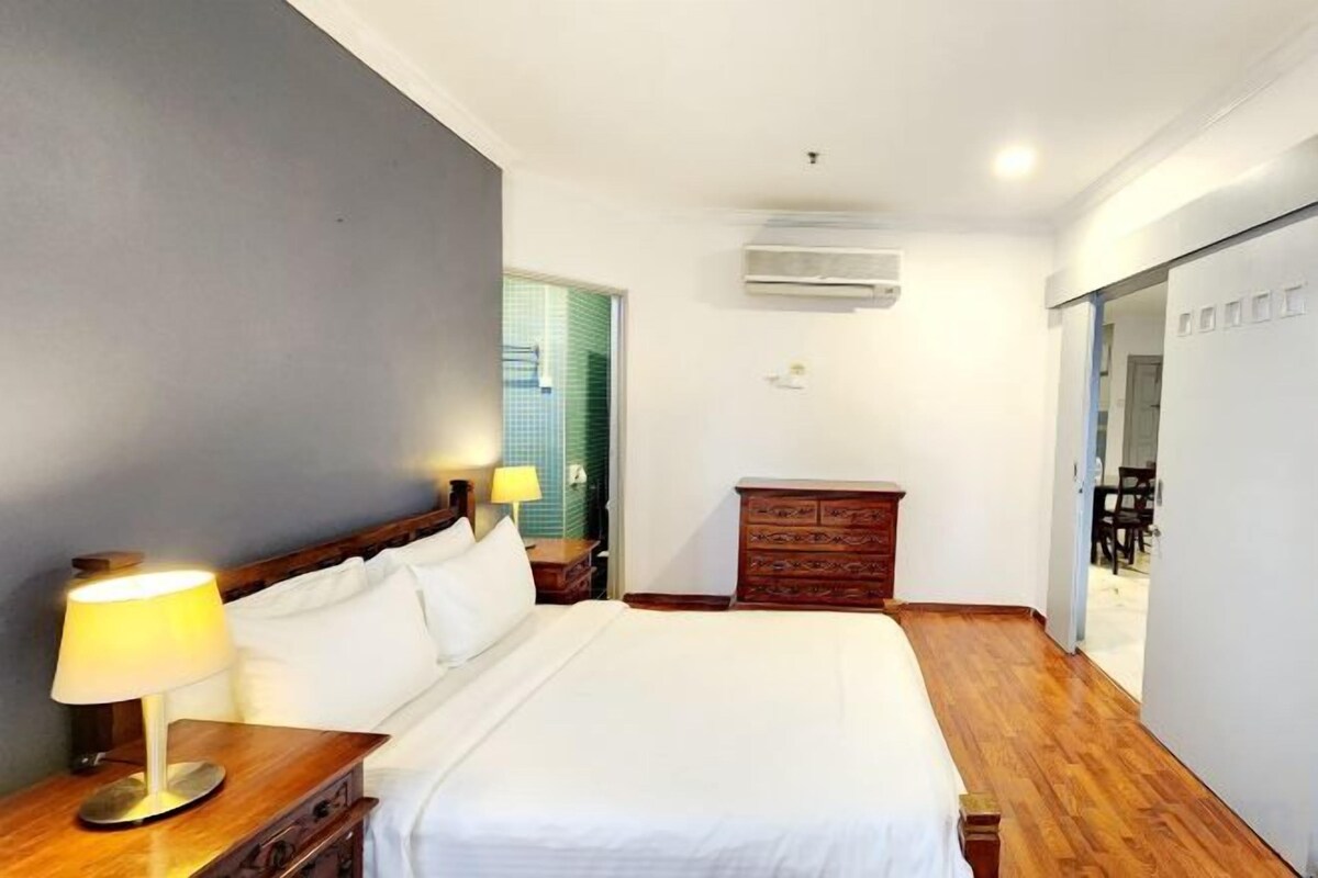 Habitación de hotel con una cama, lámparas de noche, un tocador y un aire acondicionado.