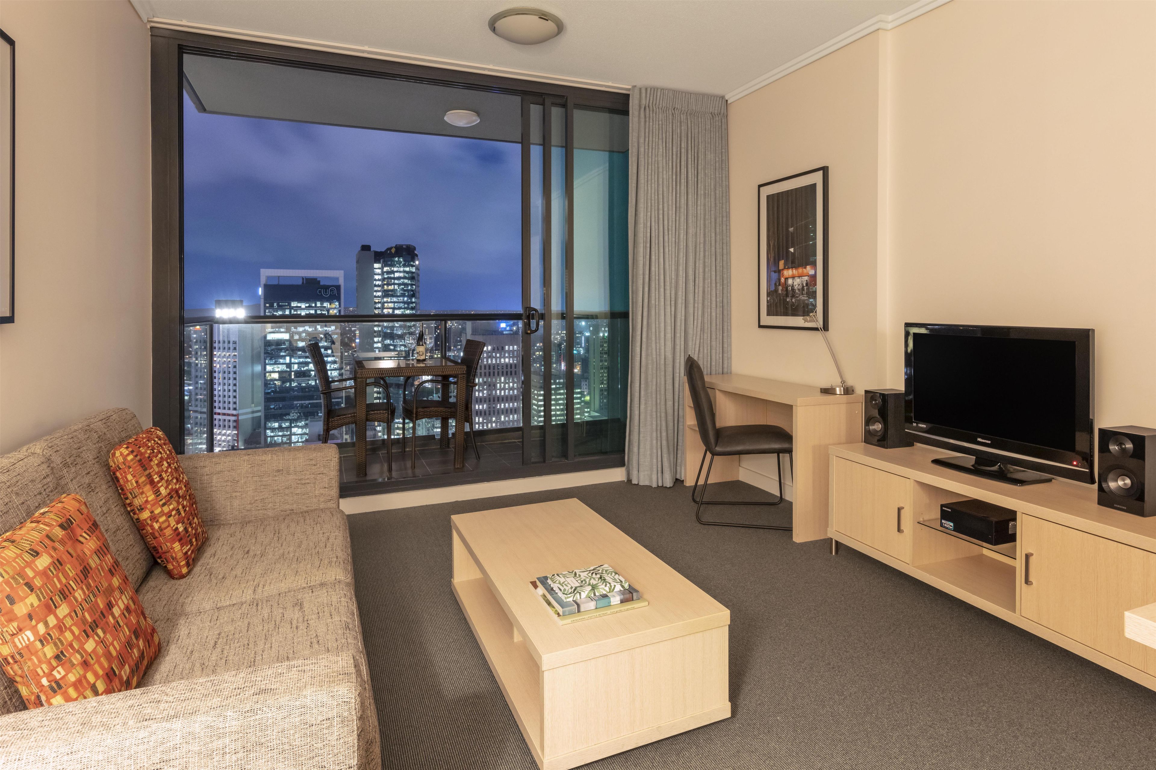 A hotel room with a balcony, a sofa, a coffee table, a TV, and a desk.