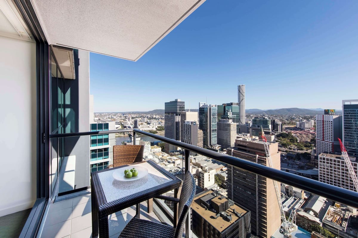 Een balkon met een tafel en stoelen, met uitzicht op een stadsbeeld met verschillende gebouwen en een heldere lucht.