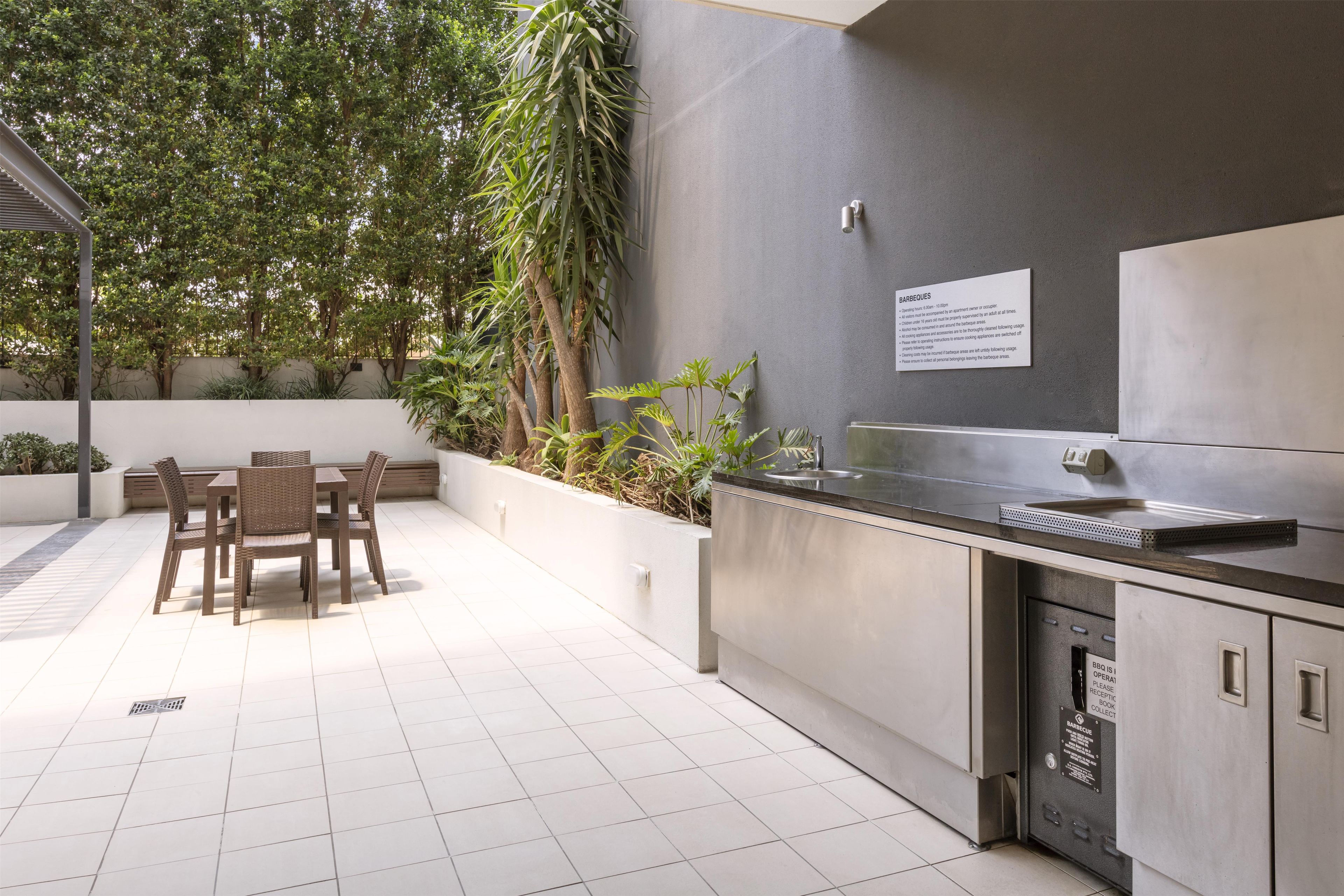 An outdoor patio with a dining table and chairs, surrounded by plants and trees.