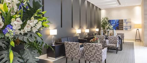 Un moderno vestíbulo de hotel con mostrador de recepción, zona de estar y un gran arreglo floral.
