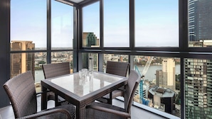 A high-rise room with a large window overlooking a cityscape, a glass-top table, and wicker chairs. - Oaks Brisbane on Charlotte Suites (Brisbane)