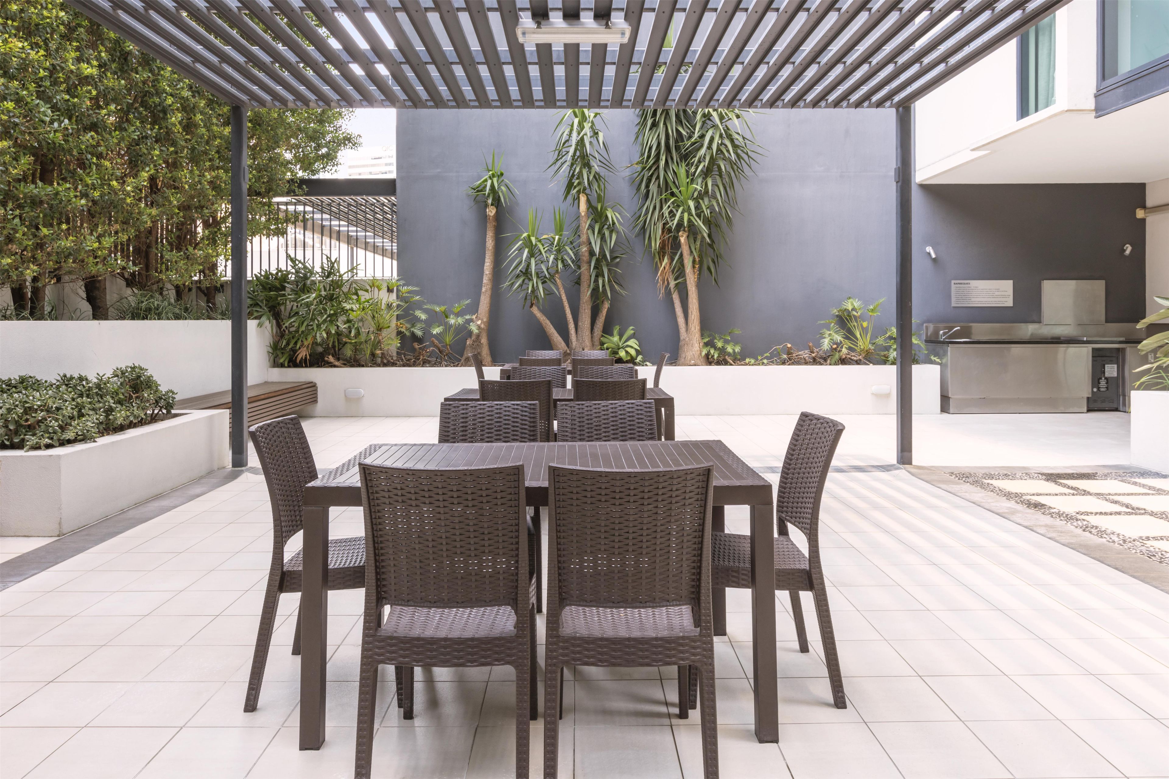 An outdoor patio with a table and chairs, surrounded by plants and a pergola.