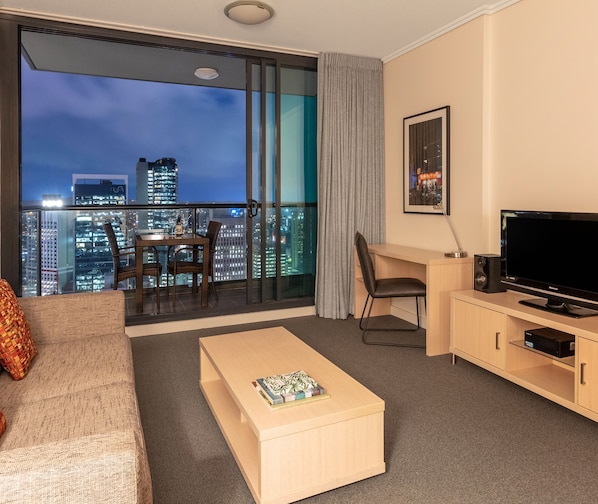 Una habitación de hotel con balcón, televisión, escritorio y sofá.