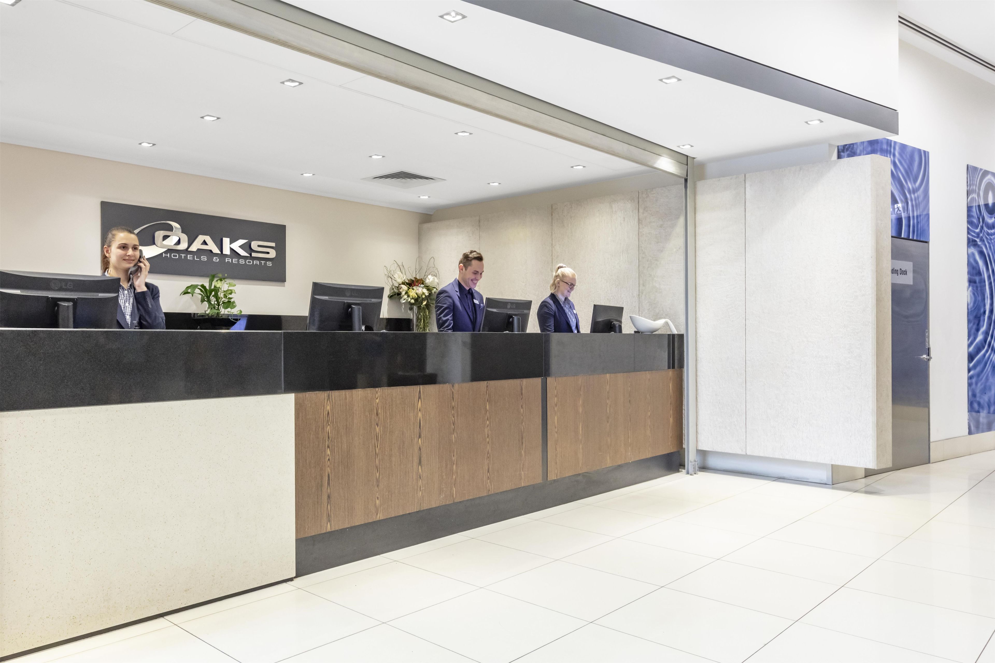 A reception desk with a sign for 'OAKS Hotels & Resorts,' three staff members, and a 'Loading Dock' sign.