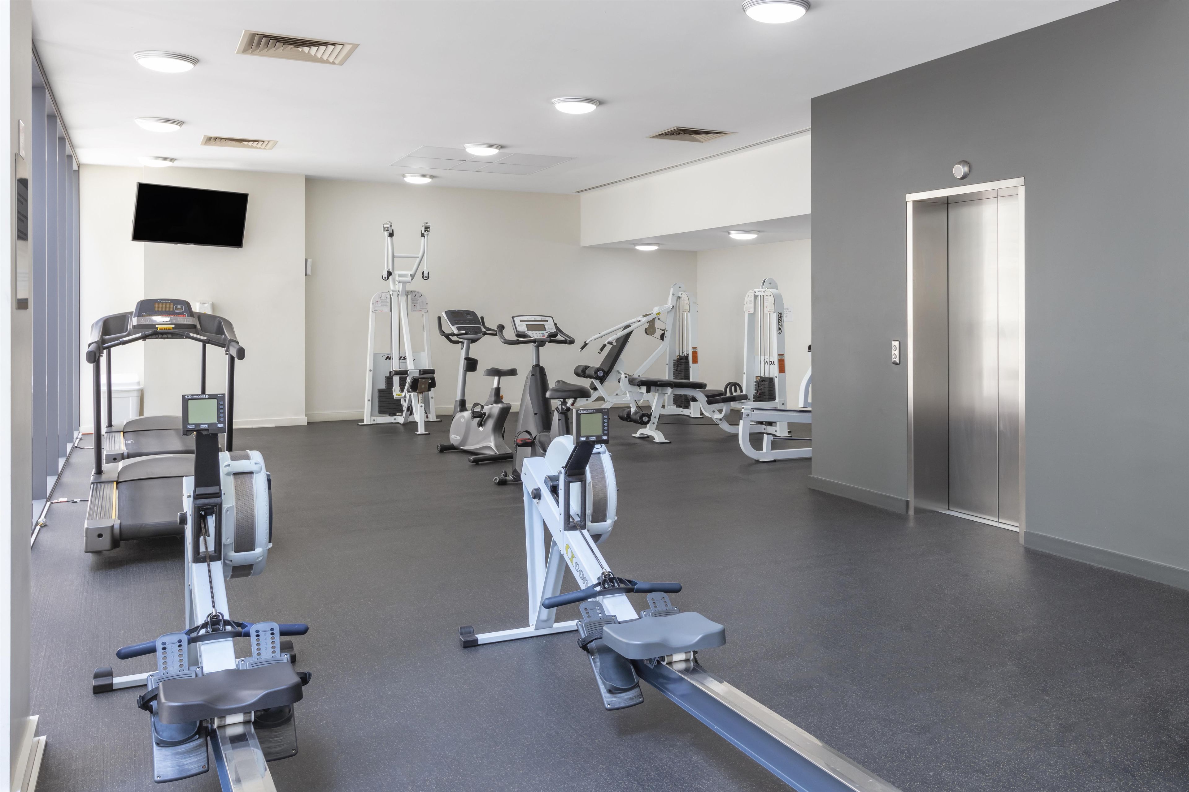 A gym with various exercise machines, a flat-screen TV, and a door.