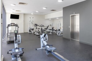 A gym with various exercise machines, a flat-screen TV, and a door.