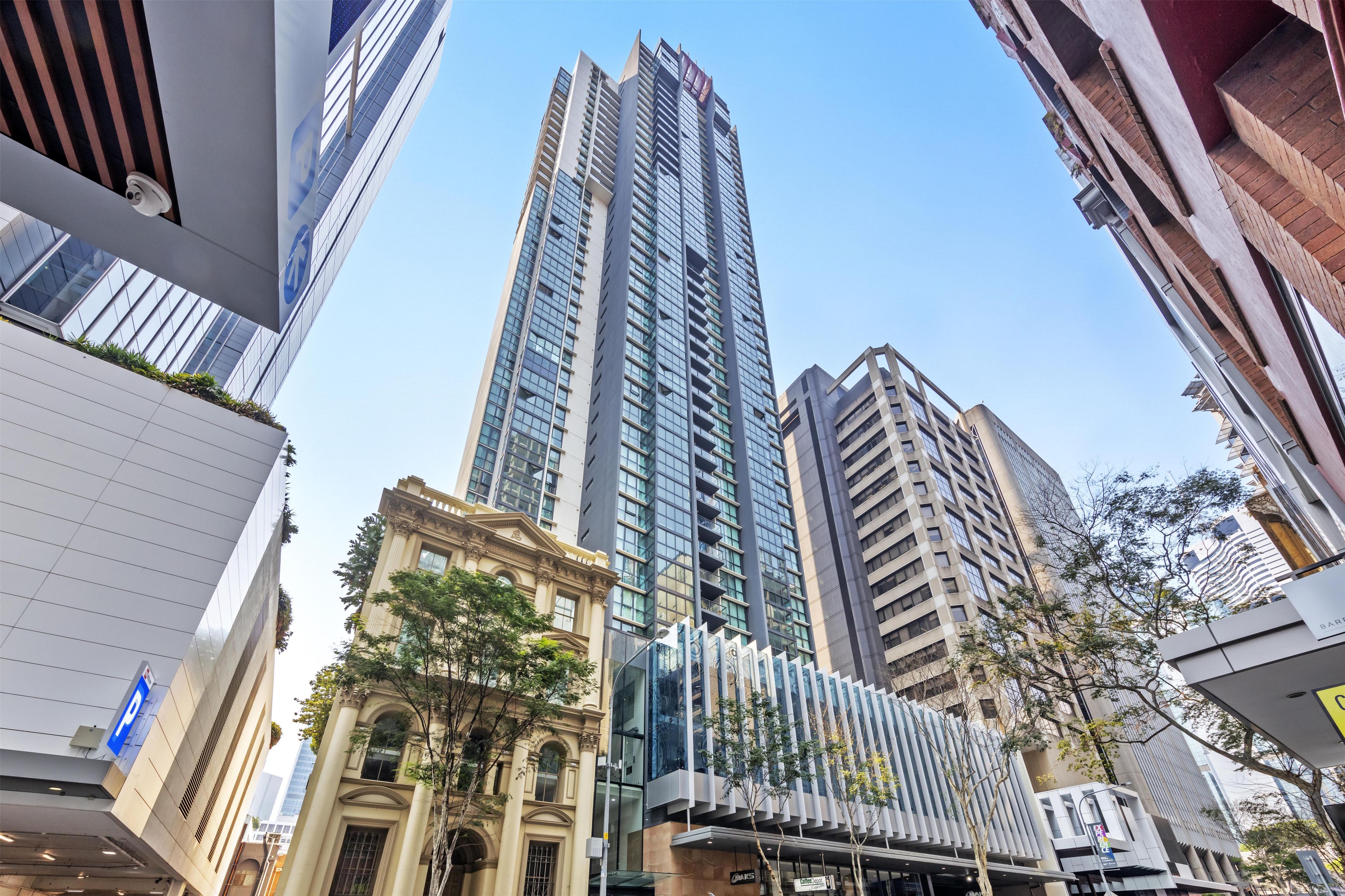 Un immeuble moderne de grande hauteur, doté d’une façade en verre, entouré d’autres bâtiments présentant différents styles architecturaux.
