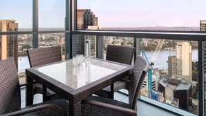 A high-rise room with a glass table and wicker chairs, offering a city view. - Oaks Brisbane on Charlotte Suites (Brisbane)
