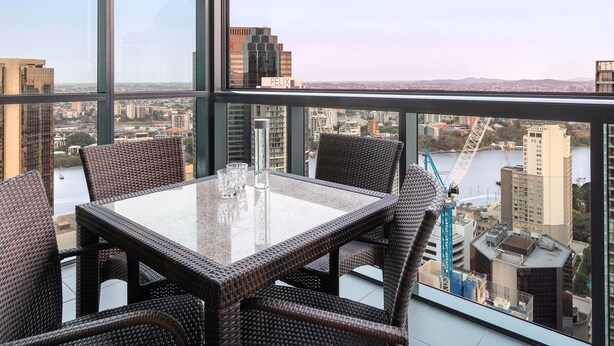 Habitación en un edificio alto con una mesa de vidrio y sillas de mimbre, con vista a la ciudad.