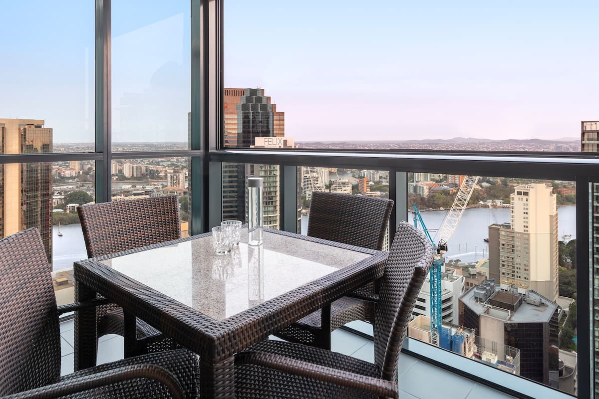 Een hoog gelegen kamer met een glazen tafel en rieten stoelen, met uitzicht op de stad.