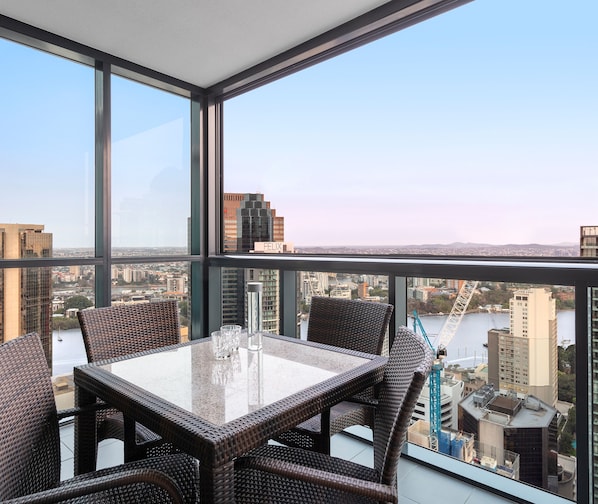 A high-rise room with a glass table and wicker chairs, offering a city view.