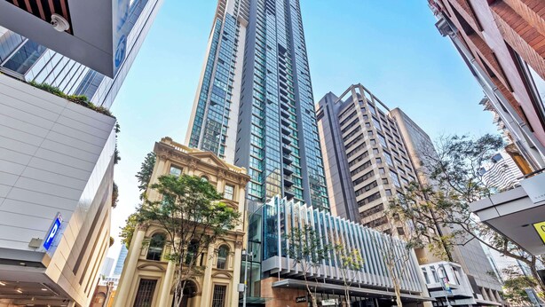 A high-rise building with a modern glass facade, surrounded by other buildings of varying architectural styles. - Oaks Brisbane on Charlotte Suites (Brisbane)