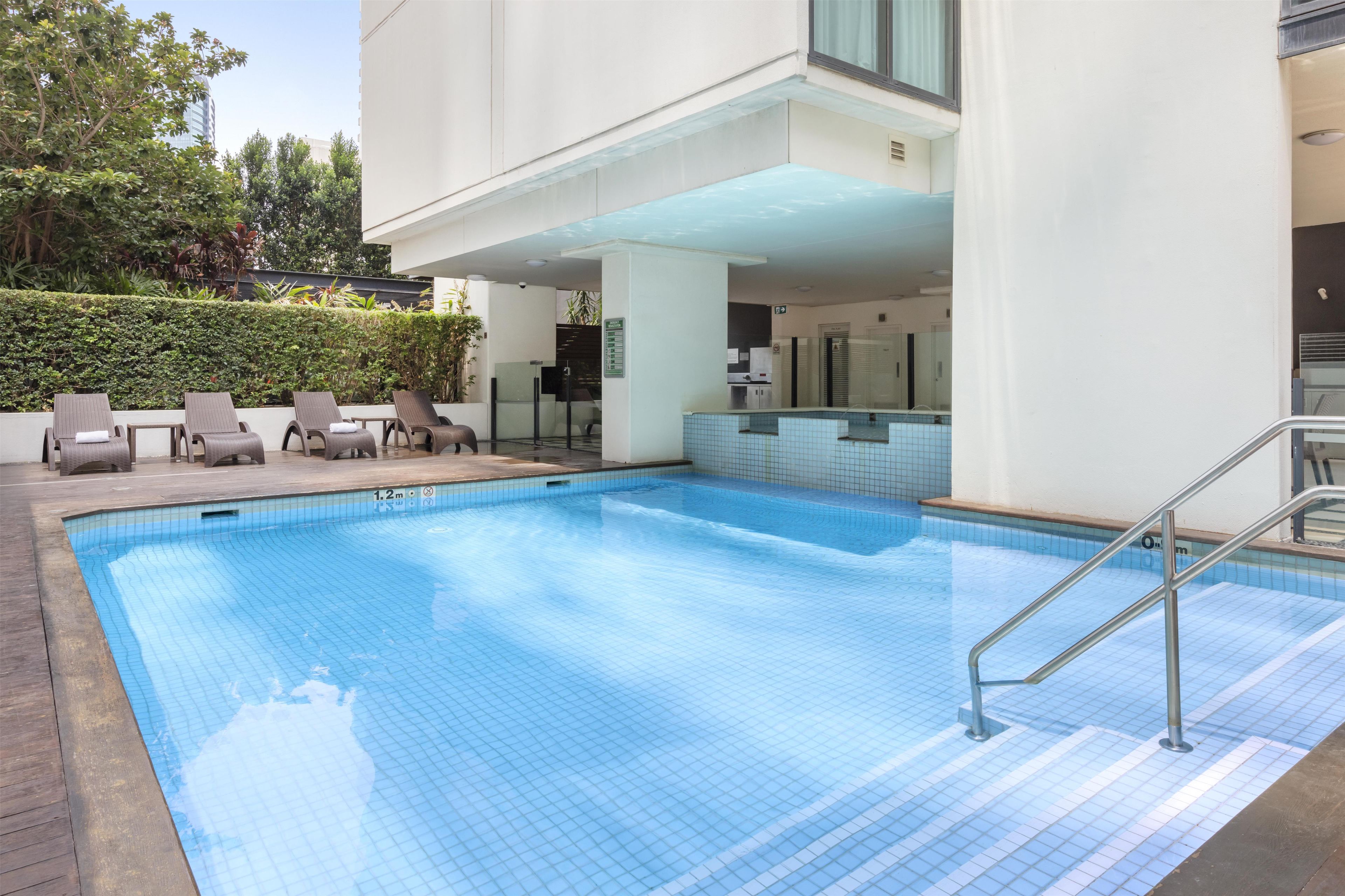 A swimming pool with a tiled deck, lounge chairs, and a glass door leading to a building.