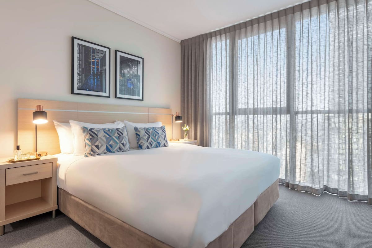 Een hotelkamer met een groot bed, twee nachtkastjes met lampen, een hoofdbord en twee ingelijste foto's aan de muur.