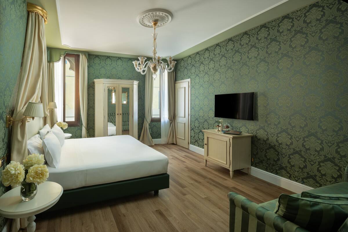 Ein Schlafzimmer mit einem großen Bett, einem Fernseher, einem kleinen Tisch mit Blumen und einem Schrank.