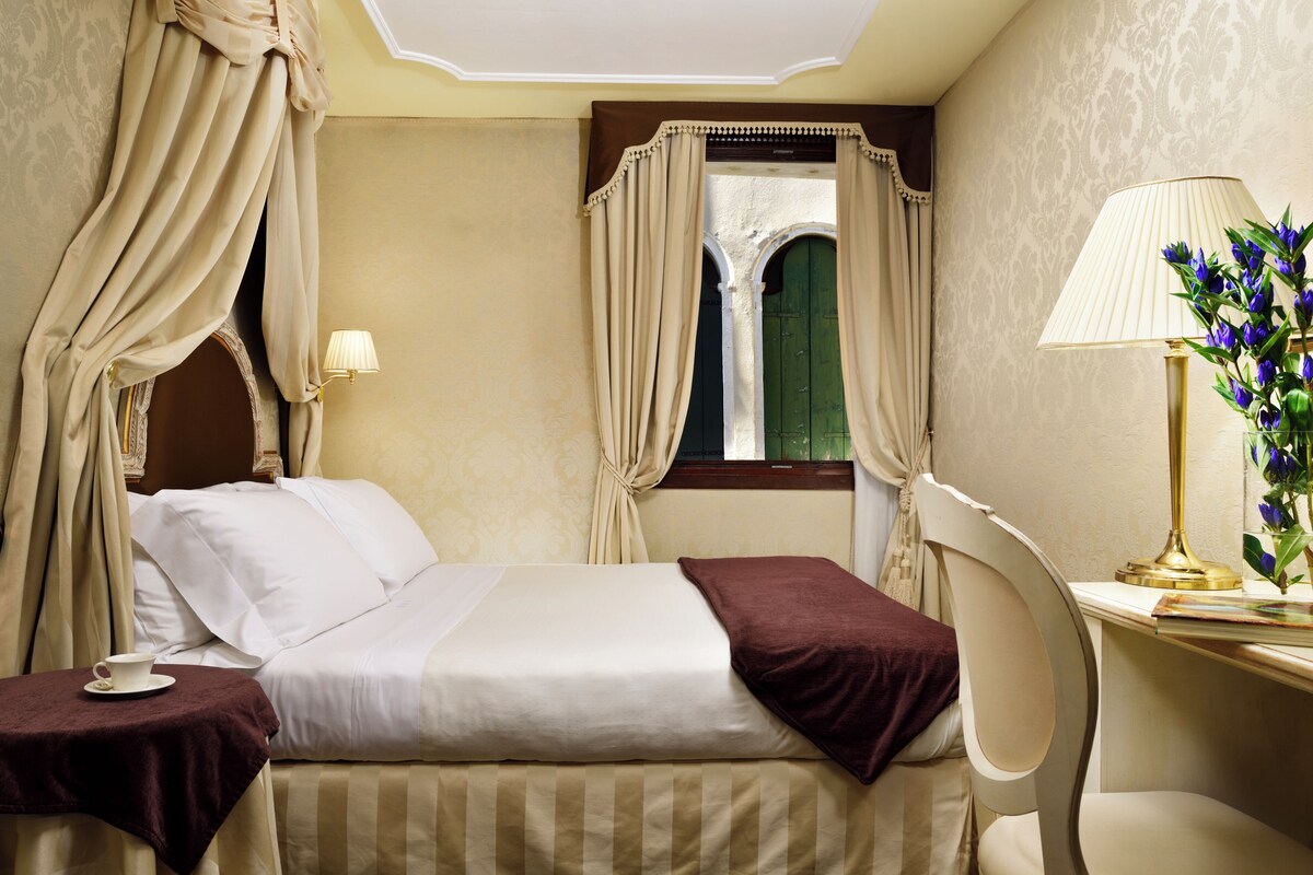 Une chambre d’hôtel avec un lit, des rideaux, une lampe et une fenêtre.