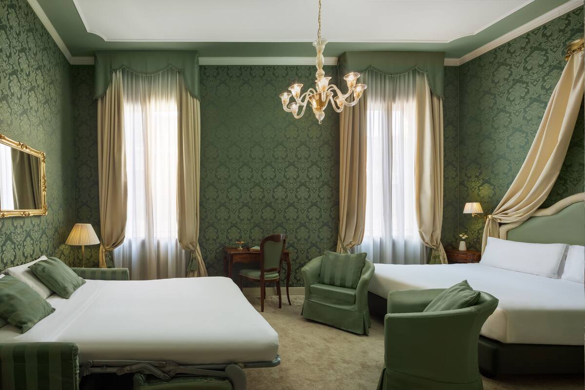 Ein Hotelzimmer mit zwei Betten, einer Kristallleuchtre und Wandpapier mit grünem Muster.