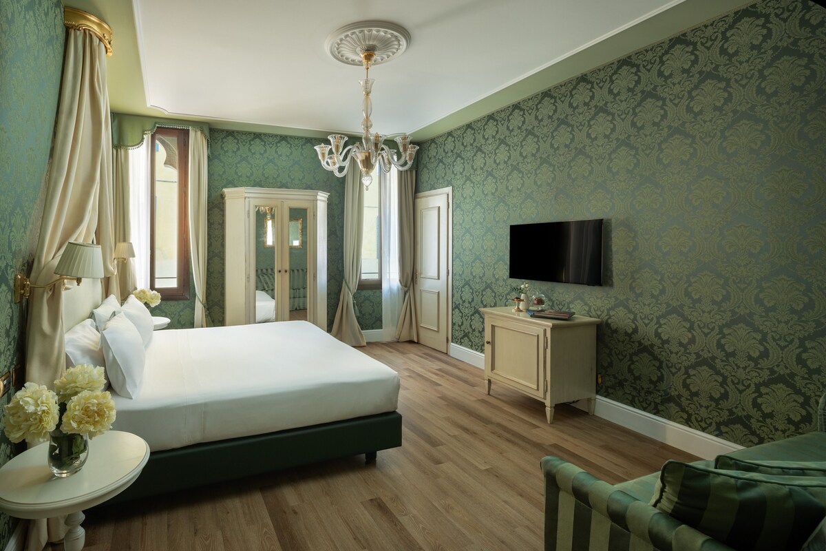 Une chambre à coucher avec un grand lit, une télévision, une petite table ornée de fleurs et un meuble.