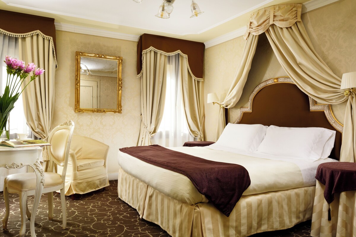 Une chambre d’hôtel avec un grand lit, un coin salon avec un fauteuil, un bureau et un miroir.