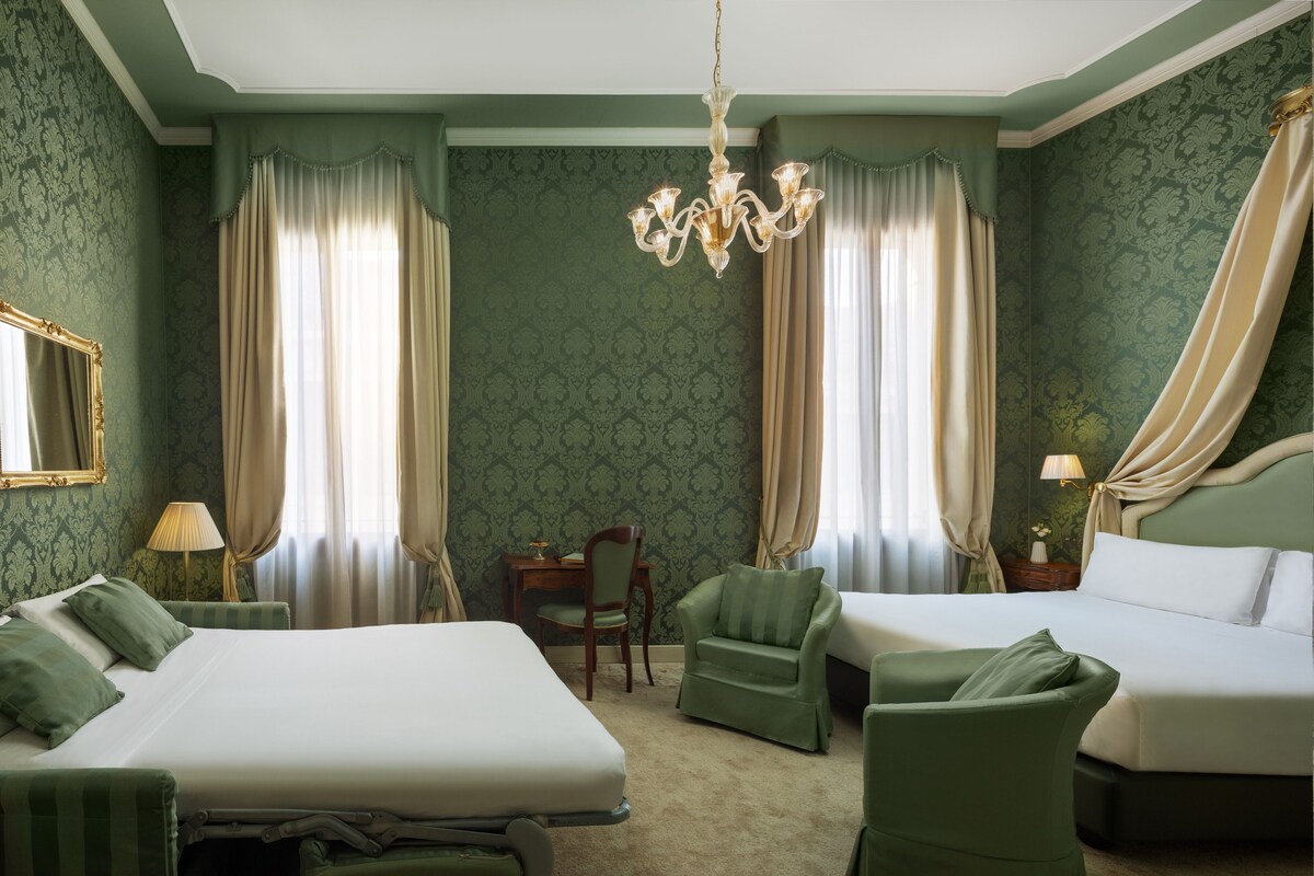 Une chambre d’hôtel avec deux lits, un lustre et un papier peint à motifs verts.