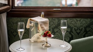 Ein Tisch mit einer Flasche, einem Glas und einem Teller mit einer Erdbeere, vor einem Fenster mit Blick auf einen Kanal und Boote.