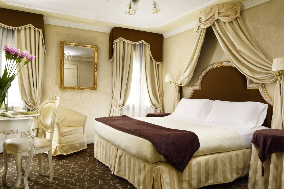 Een hotelkamer met een groot bed, een zithoek met een fauteuil, een bureau en een spiegel.