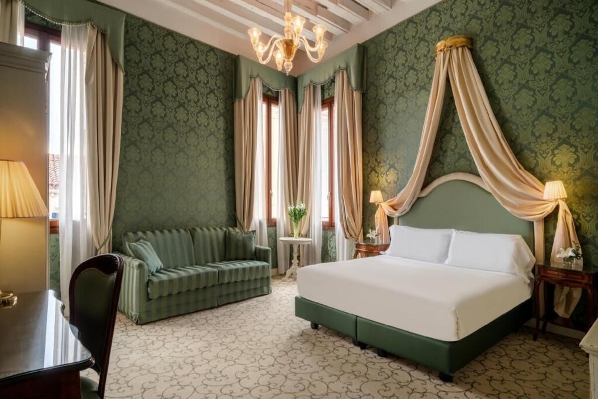Une chambre à coucher avec un lit à baldaquin, un canapé vert, une petite table et un lustre.