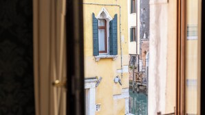 Eine schmale Straße mit Häusern an beiden Seiten, ein Fenster mit grünen Fensterläden und ein Blick auf einen Kanal.