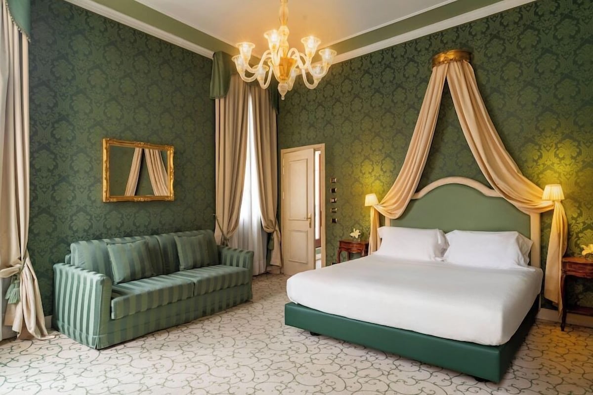 Une chambre à coucher avec un lit à baldaquin, un canapé vert, un lustre et un papier peint à motifs.