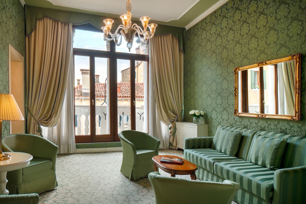 Ein Zimmer mit einem grünen Sofa, zwei Sesseln, einem runden Tisch und einer Deckenleuchte.
